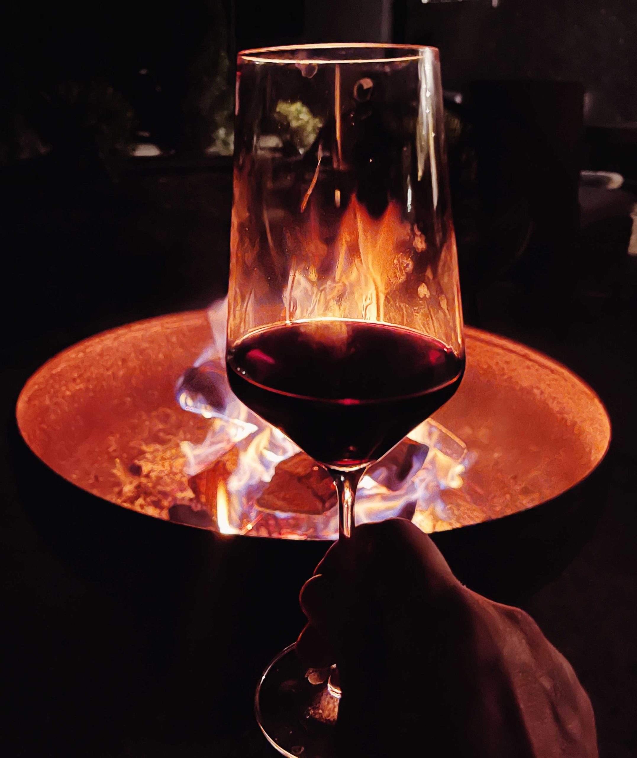 Holding a glass of red wine up with a fire pit in the background